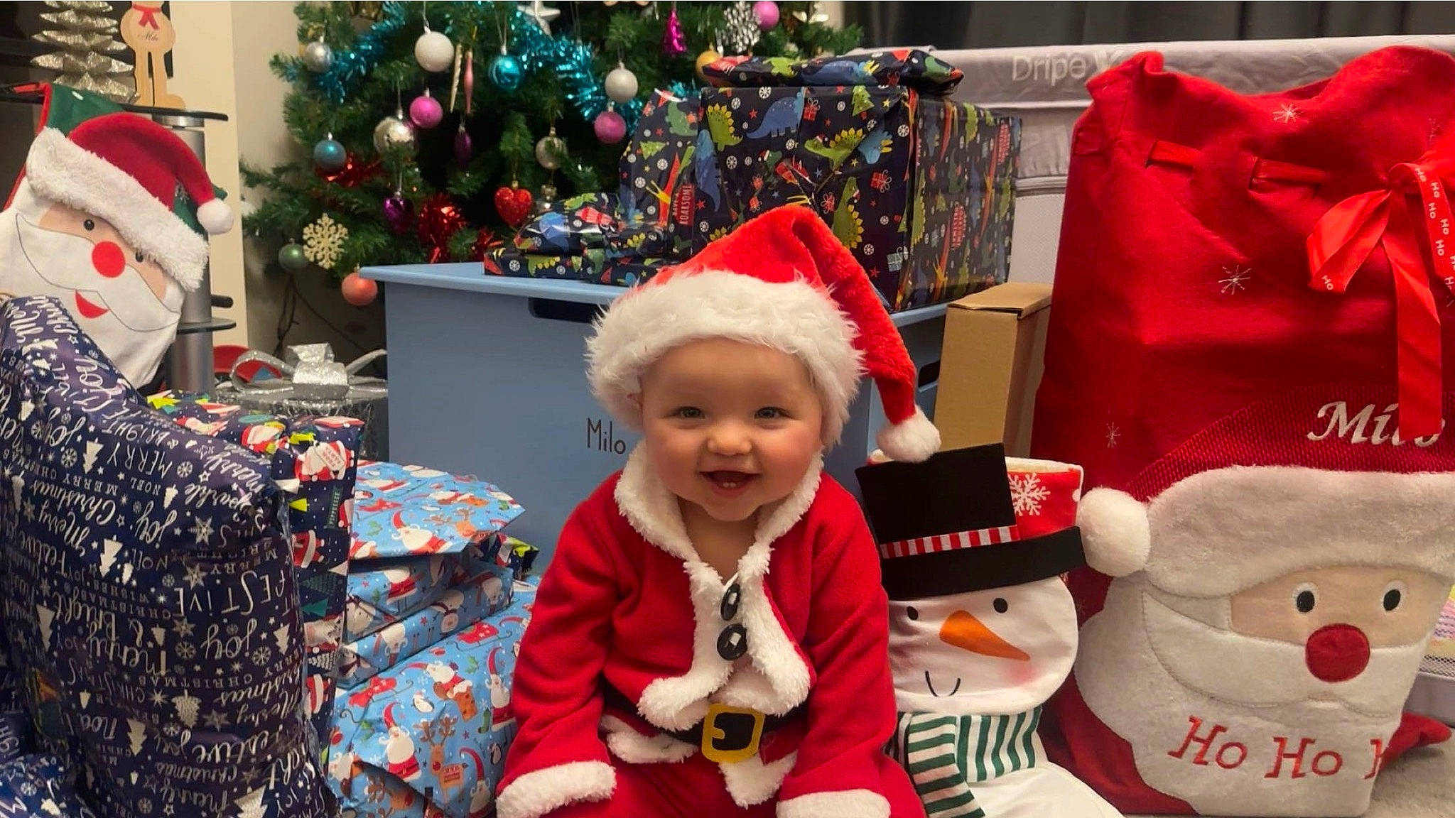 Milo is registered to the contest to win money with this photo: baby_toddler_clothing, child, christmas, christmas_decoration, christmas_eve, christmas_ornament, christmas_tree, costume_hat, event, fun, happy, headwear, holiday, joy, lap, person, red, santa_claus, smile, textile