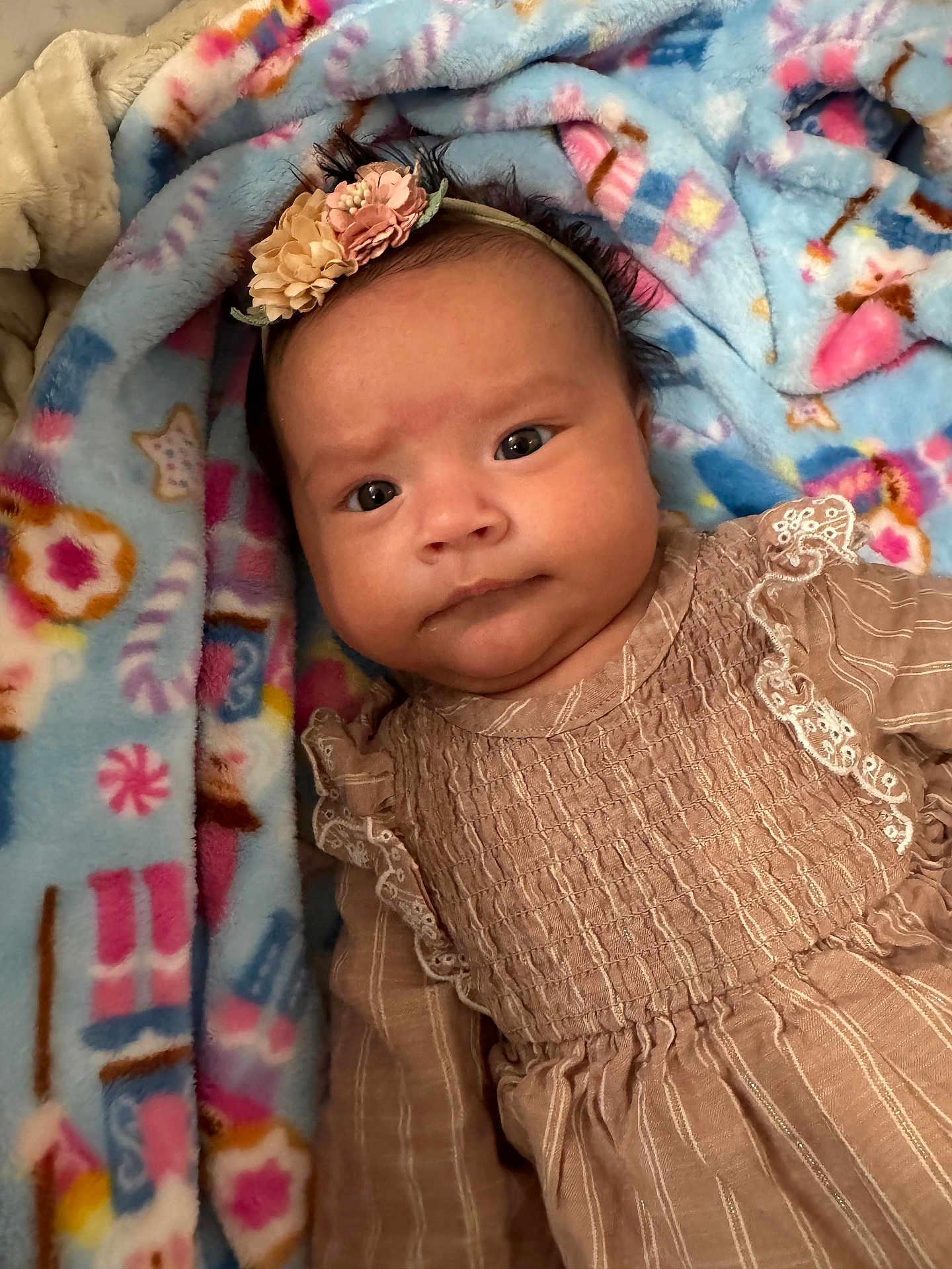 Katalina is registered to the contest to win money with this photo: baby, infant, headband, flower, dress, blanket, pattern, face, person, child, cute, indoors, soft, colorful, textile, portrait, closeup, lying_down, expression, warm