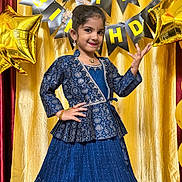 Karthika is registered to the contest to win money with this photo: child, girl, birthday, celebration, blue_dress, traditional_clothing, posing, smiling, balloons, gold_curtain, happy, festive, indoor, party, jewelry, long_skirt, decorations, smile, portrait, event