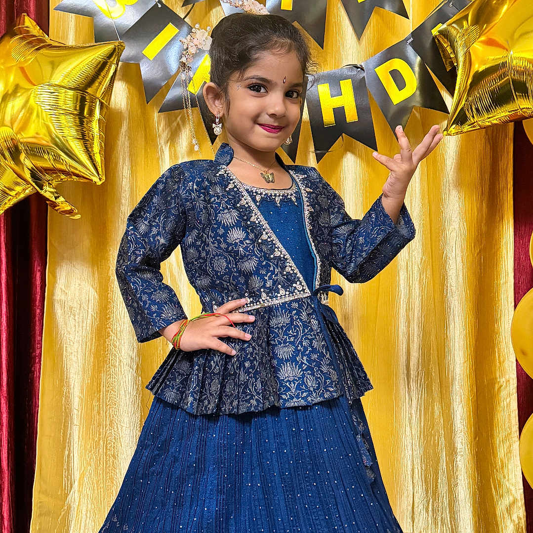 Karthika is registered to the contest to win money with this photo: child, girl, birthday, celebration, blue_dress, traditional_clothing, posing, smiling, balloons, gold_curtain, happy, festive, indoor, party, jewelry, long_skirt, decorations, smile, portrait, event