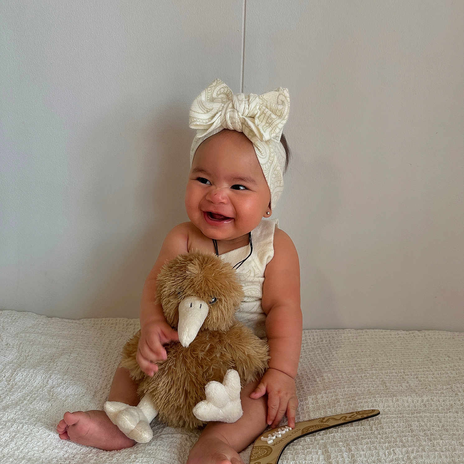 Mahlani is registered to the contest to win money with this photo: baby, barefoot, bird, blanket, bow, child, cute, happy, headband, indoors, infant, one_person, plush, portrait, sitting, smiling, soft_toy, stuffed_toy, wall, white
