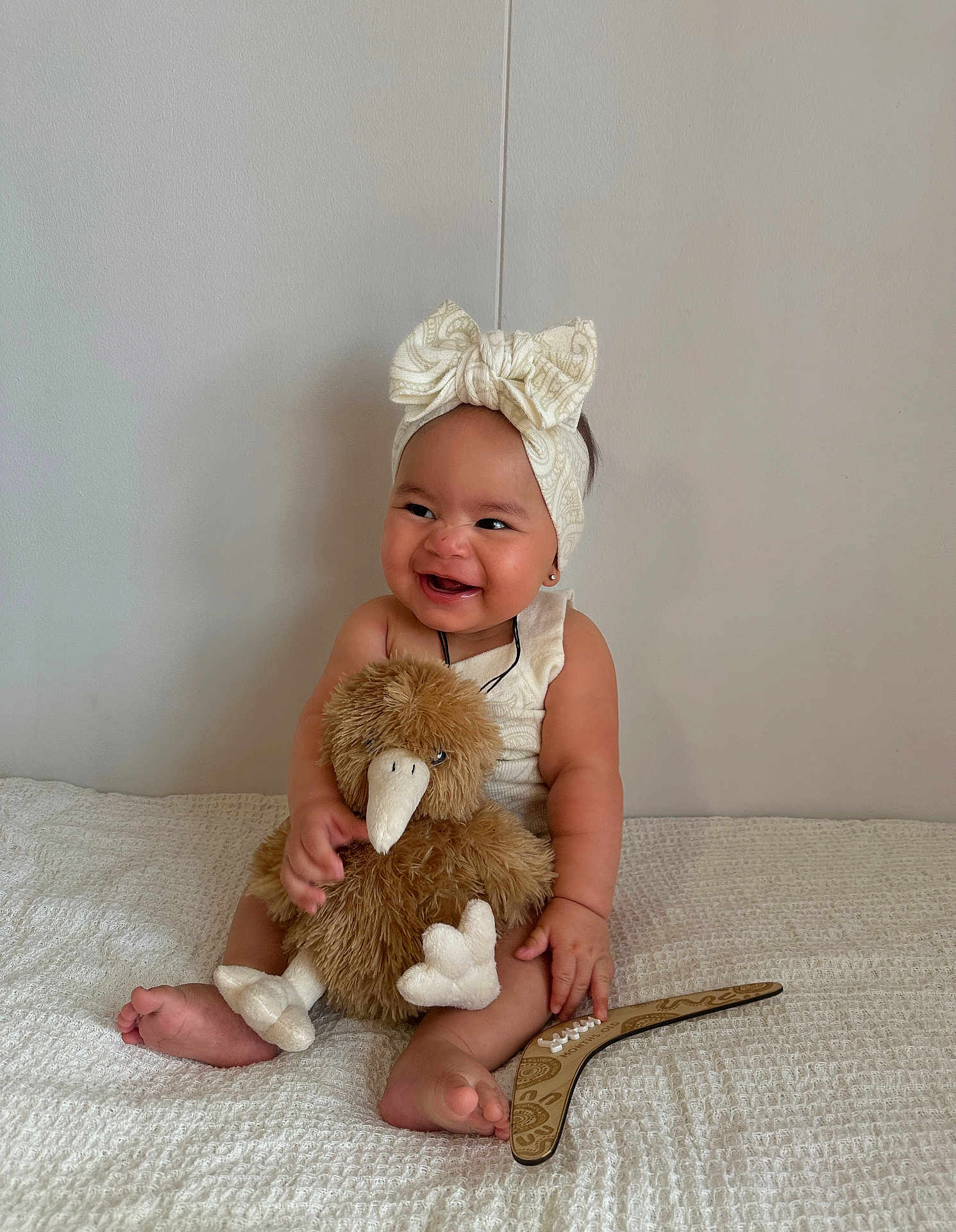 Mahlani is registered to the contest to win money with this photo: baby, child, smiling, headband, bow, stuffed_toy, plush, bird, sitting, blanket, white, happy, indoors, cute, infant, portrait, soft_toy, barefoot, one_person, wall