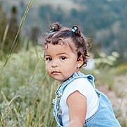 Aria joined the competition — help win amazing prizes! toddler, child, outdoor, grass, nature, denim, overalls, portrait, curly_hair, baby, cute, young_child, greenery, earrings, casual_clothing, daylight, person, small_buns, expression, side_view