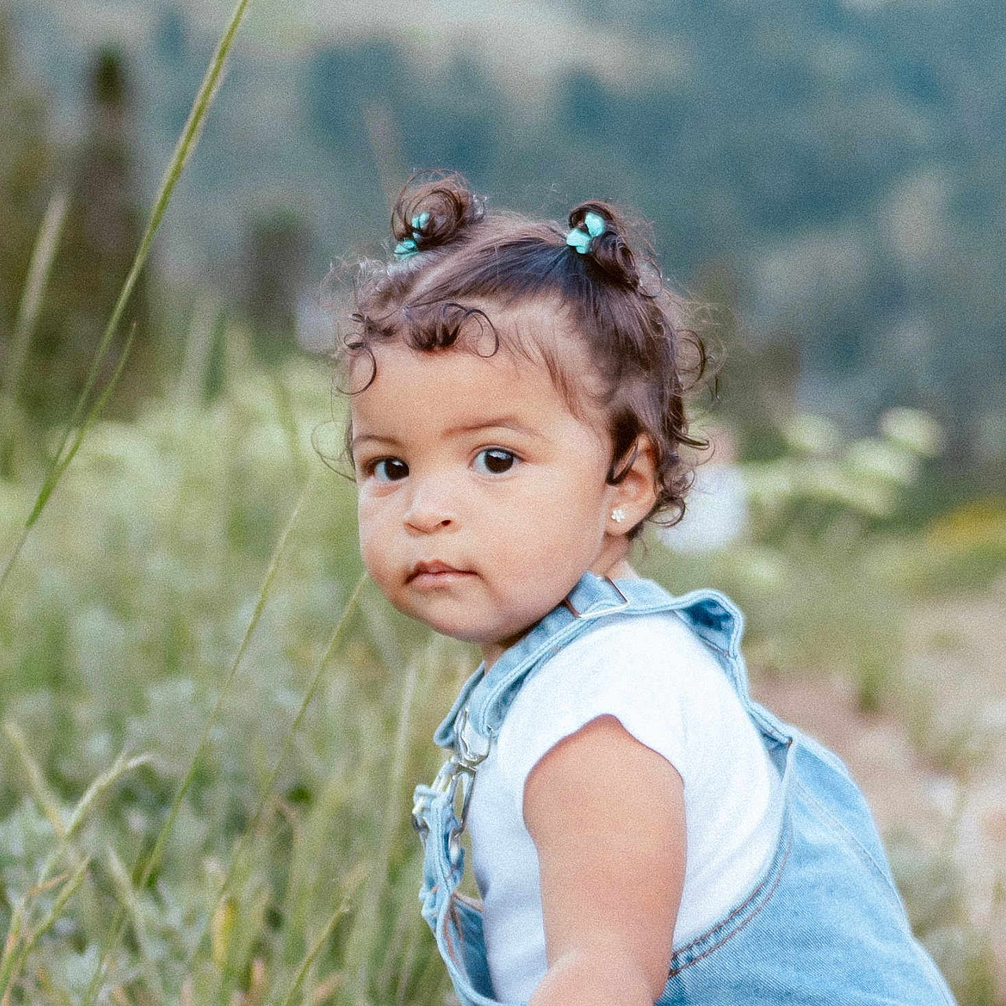 Aria joined the competition — help win amazing prizes! toddler, child, outdoor, grass, nature, denim, overalls, portrait, curly_hair, baby, cute, young_child, greenery, earrings, casual_clothing, daylight, person, small_buns, expression, side_view