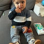 toddler, child, sitting, couch, sweater, pants, shoes, indoor, home, baby_wipes, pampers, curious, expression, furniture, clothing, footwear, person, young_child, casual, relaxed