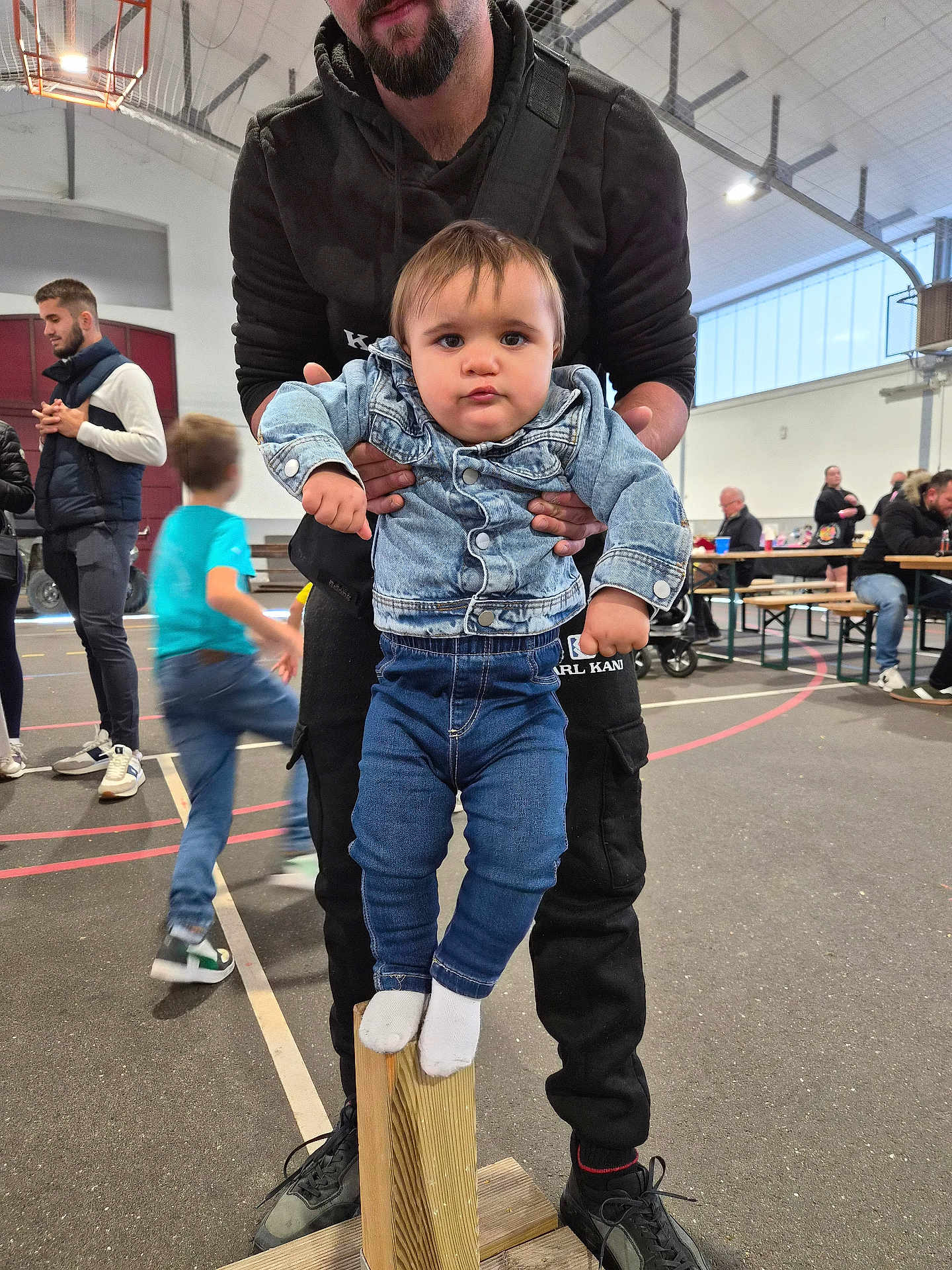 Lyzio a rejoint le concours — aidez-le/la à gagner de superbes lots ! toddler, child, man, denim_jacket, jeans, socks, wooden_block, gymnasium, indoor, people, bench, table, sports_floor, beard, hoodie, shoes, action, blurred_background, casual_clothing, family