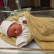 Bryan participe au concours pour gagner de l'argent avec cette photo : newborn, baby, infant, sleeping, blanket, hospital, bassinet, hat, white_clothing, towel, resting, indoors, peaceful, young_child, bed, soft_texture, medical_setting, person, cute, sleep
