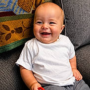 Watson is registered to the contest to win money with this photo: baby, blanket, bright, child, colorful, couch, cute, furniture, gray_shorts, happy, home, indoor, infant, playful, portrait, relaxed, seated, smiling, toy, white_tshirt