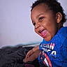 Carter is registered to the contest to win money with this photo: toddler, child, smiling, happy, blue_shirt, captain_america, bed, blanket, indoor, portrait, face, person, clothing, sitting, tongue_out, hair, skin, young_child, casual, home