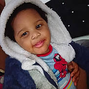 Carter is registered to the contest to win money with this photo: child, toddler, hood, jacket, smile, face, hand, person, bed, headboard, cozy, clothing, indoor, portrait, happy, warm, cute, fuzzy, colorful, young