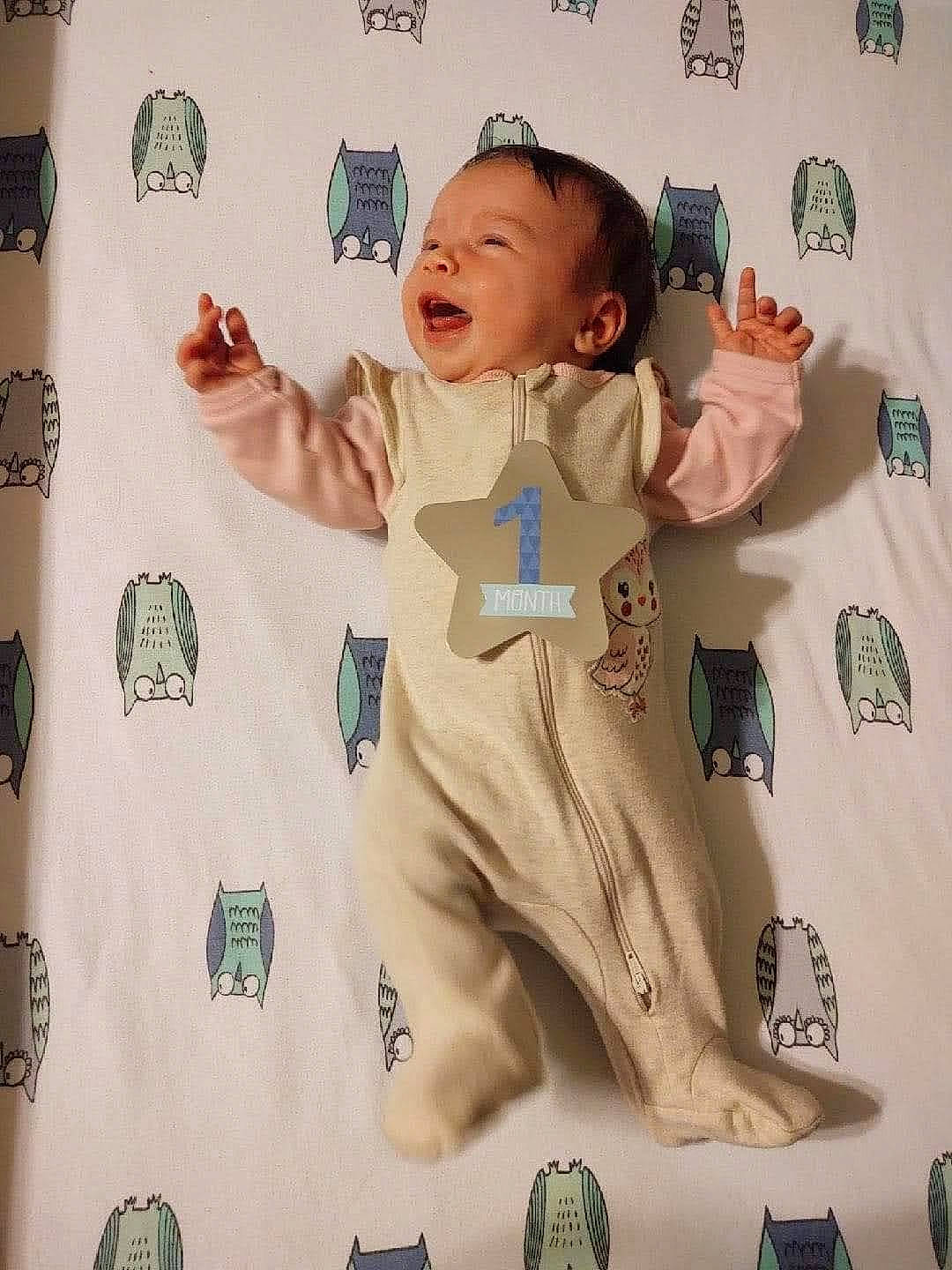 June is registered to the contest to win money with this photo: arm, baby, baby_products, baby_toddler_clothing, child, face, font, gesture, happy, head, linens, outerwear, pattern, person, room, sleeve, t_shirt, textile, thumb, toddler