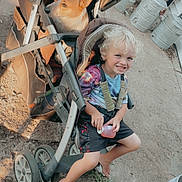 Johnny joined the competition — help win amazing prizes! child, dog, stroller, barefoot, outdoor, curly_hair, smiling, bottle, casual_clothing, metal_container, wood_pile, ground, sunlight, happy, playful, pet, summer, seatbelt, baby_stroller, curious