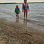 child, children, life_jacket, water, lake, shore, pebbles, sand, cloudy_sky, outdoor, smiling, wet_hair, summer, play, nature, water_sports, fun, safety, person, recreation