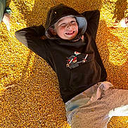 Jamey joined the competition — help win amazing prizes! child, smiling, hoodie, corn_kernels, yellow, casual_clothing, relaxed, sunlight, shadow, hand, outdoor, playful, face, person, happy, casual, childhood, leisure, young, portrait