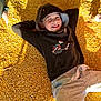 child, smiling, hoodie, corn_kernels, yellow, casual_clothing, relaxed, sunlight, shadow, hand, outdoor, playful, face, person, happy, casual, childhood, leisure, young, portrait