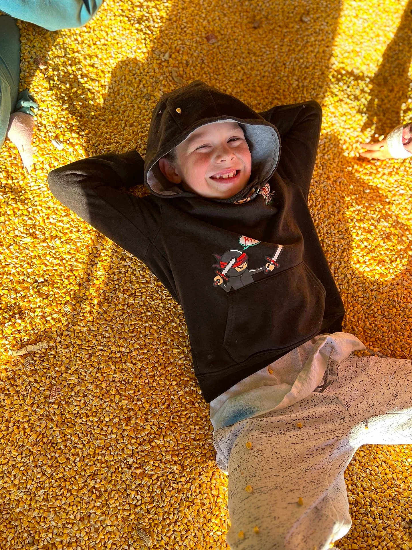 Jamey joined the competition — help win amazing prizes! child, smiling, hoodie, corn_kernels, yellow, casual_clothing, relaxed, sunlight, shadow, hand, outdoor, playful, face, person, happy, casual, childhood, leisure, young, portrait