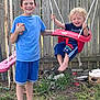 Jamey is registered to the contest to win money with this photo: backyard, barefoot, blue_shirt, boy, child, curly_hair, fence, fun, garden, grass, happy, holding, outdoor, play, shorts, smile, sneakers, sunny, swing, toy