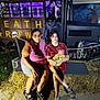 woman, child, baby, hay_bale, halloween, decoration, skeleton, costume, night, outdoor, purple_light, vehicle, spooky, family, grass, concrete, person, glasses, shorts, tshirt