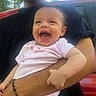 baby, laughing, smiling, infant, pink_onesie, adult_arm, black_shirt, outdoor, trees, vehicle, red_car, happy, person, holding, portrait, daylight, cute, skin, face, child