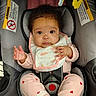 Keziah joined the competition — help win amazing prizes! baby, infant, car_seat, seatbelt, bib, pink_clothing, heart_pattern, socks, curly_hair, cute, child, sitting, safety_harness, indoor, portrait, young_child, looking_at_camera, small_hands, expression, toddler