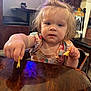 casual, child, chips, clothing, colorful, curly_hair, cute, expression, face, food, hand, high_chair, indoor, person, restaurant, sitting, table, toddler, wooden_table, young_child