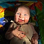 baby, beige_outfit, blue_eyes, buttoned_clothing, child, colorful_background, cute, face, hand, happy, infant, lying_down, person, playmat, portrait, shadow, skin, smiling, sunlight, young_child