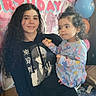 birthday, balloons, child, toddler, woman, indoor, celebration, snack, curly_hair, casual_clothing, hoodie, sneakers, banner, party, home, smile, holding, colorful, young_person, festive