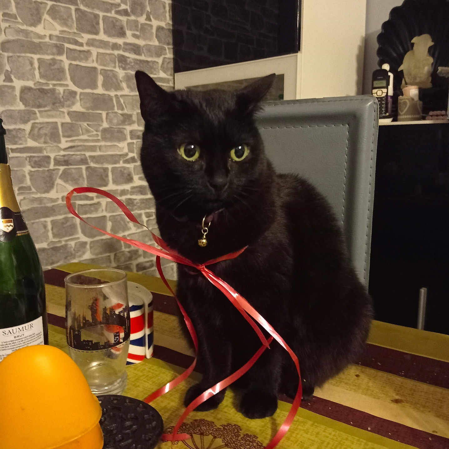 Plume participe au concours pour gagner de l'argent avec cette photo : black_cat, cat, pet, animal, green_eyes, bell_collar, red_ribbon, sitting, table, indoor, home, dining_room, chair, stone_wall, bottle, glass, hat, tablecloth, portrait, photography