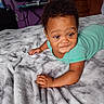 Kamari joined the competition — help win amazing prizes! baby, child, infant, portrait, smiling, lying_down, bed, blanket, bedroom, green_clothing, striped_clothing, curly_hair, brown_skin, face, eyes, hands, indoor, furniture, cozy, photography