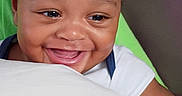 Kamari joined the competition — help win amazing prizes! baby, child, smiling, happy, portrait, face, head, curly_hair, eyes, mouth, teeth, sitting, indoor, cushion, shirt, white_clothing, close_up, joyful, infant, person