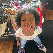 Musik is registered to the contest to win money with this photo: child, curly_hair, tongue_out, silly_face, standing, bed, blanket, stuffed_animal, rug, wooden_floor, clothing, jeans, socks, indoor, playful, happy, person, casual, young, fun