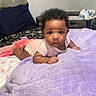 baby, infant, tummy_time, blanket, bed, pillow, curly_hair, indoor, child, cute, pink_clothing, face, person, looking, resting, soft_texture, home, cozy, portrait, young