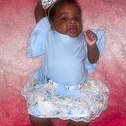 Essence is registered to the contest to win money with this photo: baby, child, infant, lying_down, pink_background, blue_clothing, floral_skirt, headband, bow, socks, cute, portrait, soft_texture, indoor, person, smiling, happy, young_child, fashion, closeup