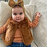 baby, child, infant, headband, bow, vest, fur, jeans, orange_top, smile, face, couch, pillow, textured_fabric, indoor, cute, portrait, person, seated, happy
