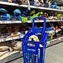 dog, shopping_basket, pet_store, pet_toys, blue, floor, shelves, stuffed_animals, plush_toys, dog_leash, dog_basket, relaxed, white_dog, store_aisle, shopping_cart, pet_accessories, indoor, retail, pets, animal