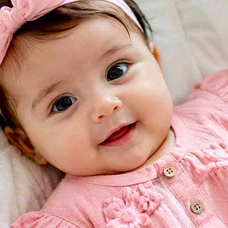 Hijen is registered to the contest to win money with this photo: baby, infant, child, portrait, face, smiling, eyes, pink_clothing, floral_outfit, hair_bow, headband, lying_down, close_up, indoor, soft_lighting, happy, cute, baby_clothes, button, photography