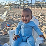 baby, child, smile, blue_clothing, beach, sand, plastic_chair, palm_trees, sunny_day, outdoor, happy, person, toy, footwear, people, sky, vacation, relaxation, play, summer