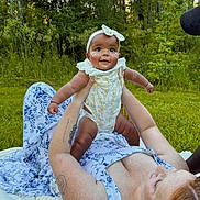 Makiyah is registered to the contest to win money with this photo: baby, woman, outdoor, grass, trees, blanket, headband, smiling, holding, nature, tattoo, dress, freckles, happy, playful, person, greenery, sunlight, child, family