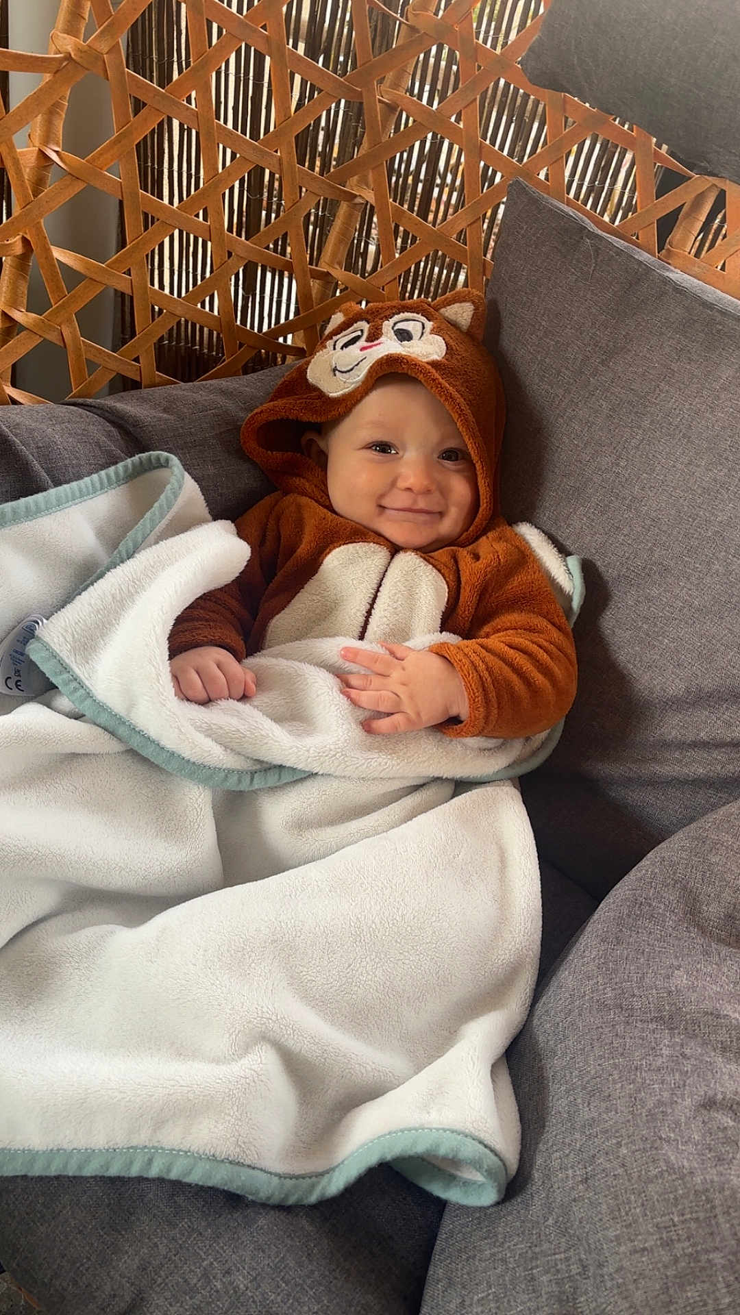 Jayden a rejoint le concours — aidez-le/la à gagner de superbes lots ! baby, child, hoodie, blanket, smile, face, cushion, chair, indoor, cozy, cute, animal_costume, wooden_background, soft, warm, infant, portrait, happy, seated, clothing