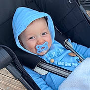 Jayden a rejoint le concours — aidez-le/la à gagner de superbes lots ! baby, beads, black_canopy, blanket, blue_clothing, cozy, eyes, face, hand, hood, hooded_jacket, infant, outdoor, pacifier, pacifier_clip, portrait, seat_belt, smile, stroller, wooden_deck