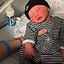 newborn, baby, sleeping, striped_clothing, hat, nike, infant, hospital_bed, bottle, hand, adult, rest, cute, cozy, soft_lighting, blanket, person, footwear, black_hat, baby_booties