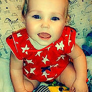 Kahleesi Lynn is registered to the contest to win money with this photo: baby, child, smiling, red_clothing, stars_pattern, blue_eyes, toy, blanket, pillow, animal_prints, cute, happy, indoors, sitting, infant, soft_texture, playful, face, person, closeup