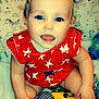 baby, child, smiling, red_clothing, stars_pattern, blue_eyes, toy, blanket, pillow, animal_prints, cute, happy, indoors, sitting, infant, soft_texture, playful, face, person, closeup