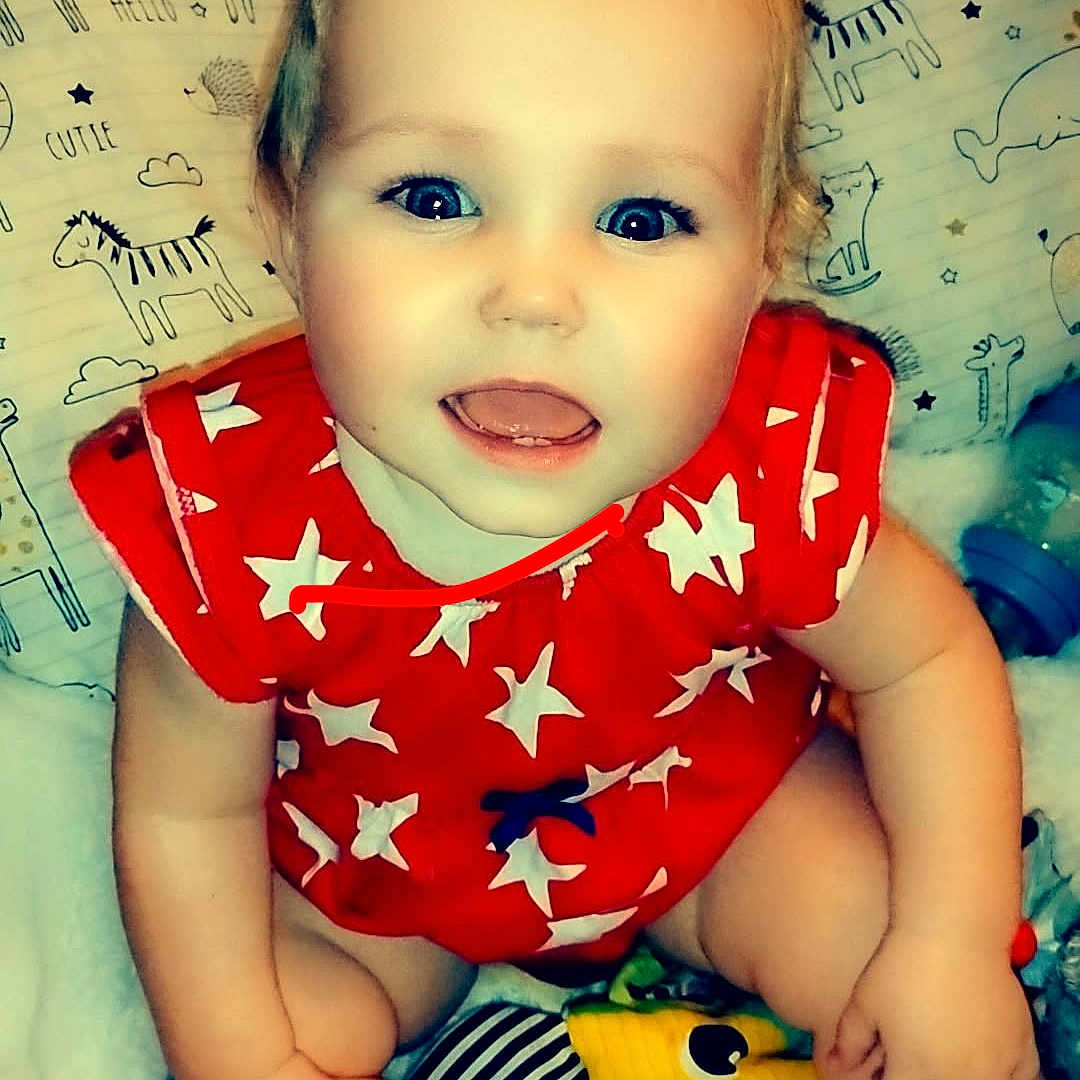 Kahleesi Lynn is registered to the contest to win money with this photo: animal_prints, baby, blanket, blue_eyes, child, closeup, cute, face, happy, indoors, infant, person, pillow, playful, red_clothing, sitting, smiling, soft_texture, stars_pattern, toy