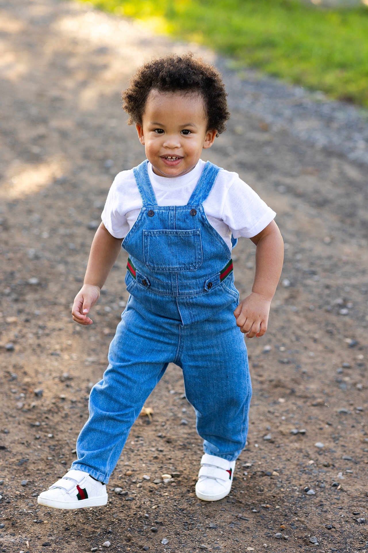 Maserati joined the competition — help win amazing prizes! toddler, child, denim_overalls, white_shirt, white_sneakers, curly_hair, smiling, outdoor, gravel_path, sunlight, happy, walking, nature, greenery, casual_clothing, cute, portrait, daylight, person, fashion