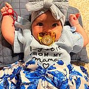 Erika joined the competition — help win amazing prizes! adorable, baby, blue_flower_skirt, bow, child, clothing, cute, fashion, hand, headband, indoors, infant, knitwear, lying_down, pacifier, pillow, portrait, smiling, text_on_clothing, texture