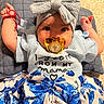 adorable, baby, blue_flower_skirt, bow, child, clothing, cute, fashion, hand, headband, indoors, infant, knitwear, lying_down, pacifier, pillow, portrait, smiling, text_on_clothing, texture
