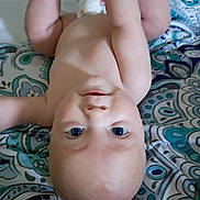 Jacob is registered to the contest to win money with this photo: baby, infant, child, upside_down, blue_eyes, bare_chest, arms_raised, blanket, patterned_blanket, cute, playful, skin, face, head, lying_down, indoors, closeup, adorable, expression, young_child