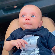 Jorge is registered to the contest to win money with this photo: baby, infant, blue_eyes, tshirt, cartoon_bear, lap, person, car_interior, tattoo, hand, cute, child, portrait, casual_clothing, skin, head, sitting, expression, closeup, human
