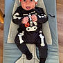Maverick is registered to the contest to win money with this photo: baby, infant, child, skeleton_costume, halloween, hat, tongue_out, bouncer, babybjorn, wooden_floor, black_clothing, white_bones, pumpkin, playful, cute, indoors, smiling, face, headwear, hands